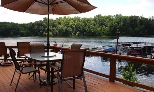 Una terraza con sillas y sombrilla con vistas a un lago con barcos atracados cerca
