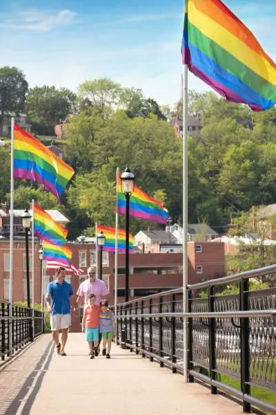 La gente camina a lo largo de un puente i galena que está forrado con banderas lgbt