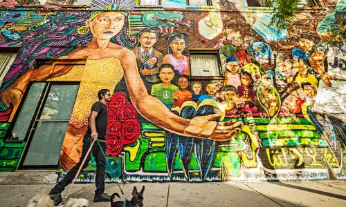 Un hombre pasea a tres perros delante de un colorido mural callejero.