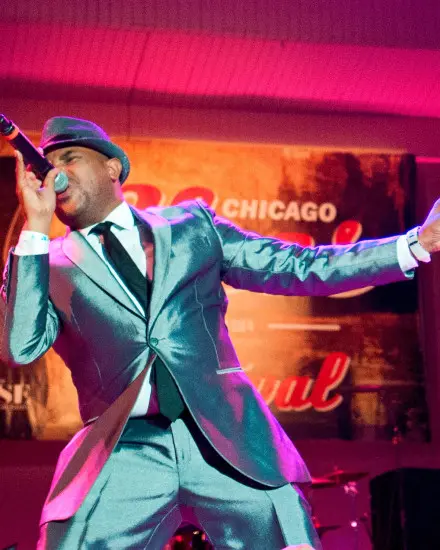 Un cantante de blues con un elegante traje metálico en el escenario cantando una canción.