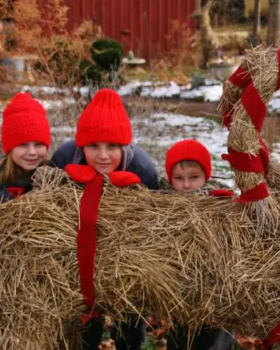 Tres niños se esconden detrás de una festiva escultura de heno