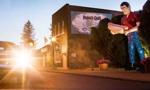 Puesta de sol detrás de un automóvil con una estatua gigante de un hombre con un perrito caliente en la mano