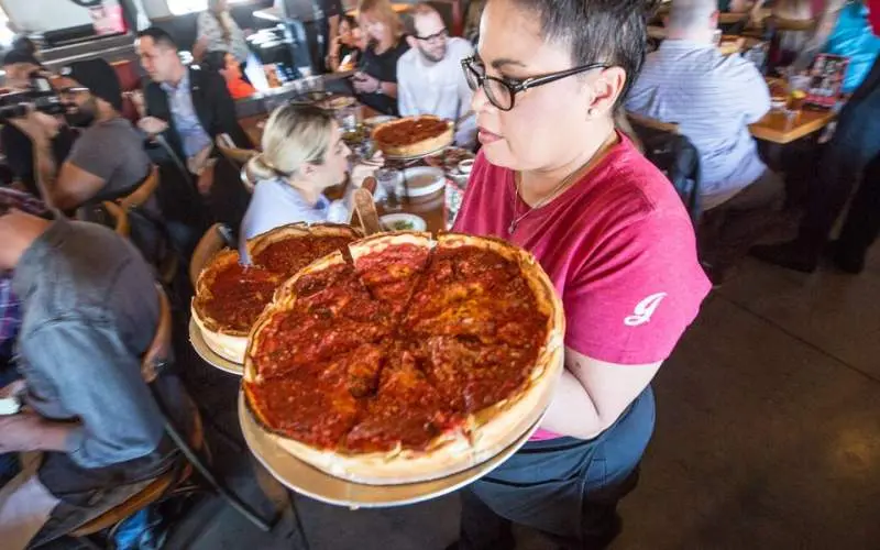 Un camarero de Giordano's lleva dos pizzas de plato hondo por un restaurante muy concurrido.