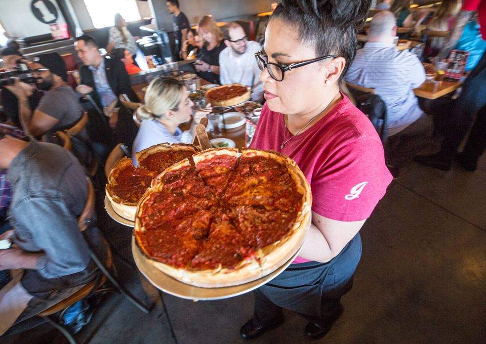 Un camarero de Giordano's lleva dos pizzas de plato hondo por un restaurante muy concurrido.