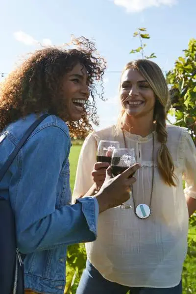 Dos chicas ríen mientras disfrutan de un vino tinto en un viñedo