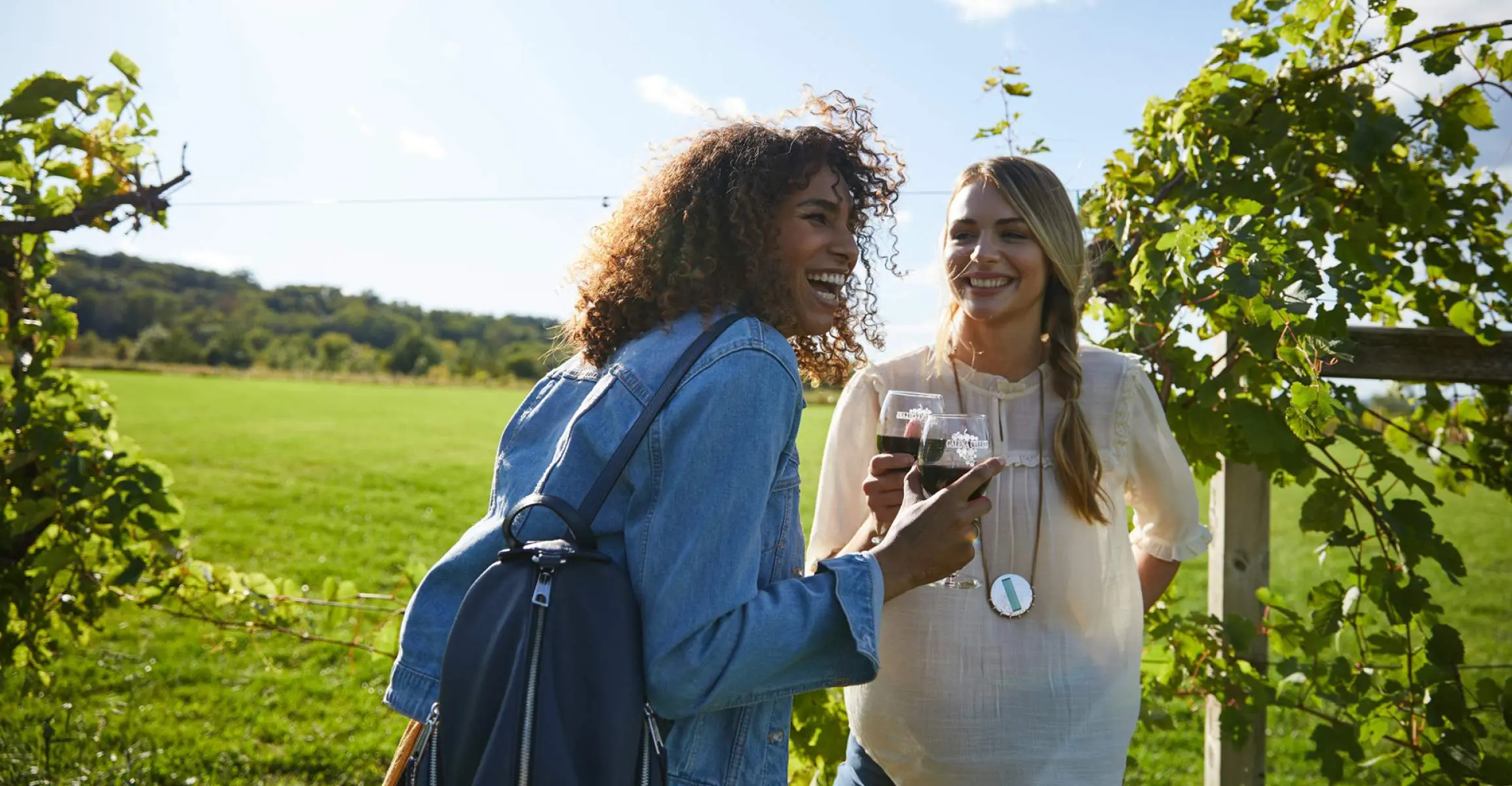 Dos chicas ríen mientras disfrutan de un vino tinto en un viñedo