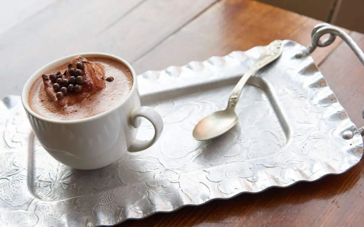 Una taza de chocolate caliente y una cucharilla sobre una bandeja de servir