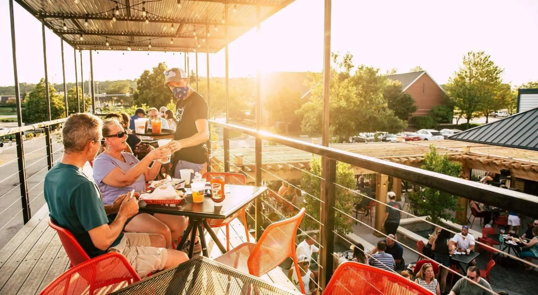 Personas a las que se sirve comida en un entresuelo soleado de un restaurante al aire libre