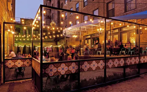 Comensales cenando en el patio exterior bajo las luces de las bombillas