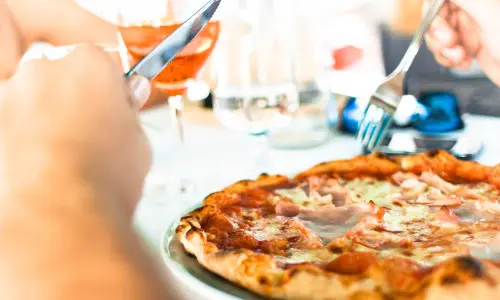 Persona comiendo pizza con cuchillo y tenedor