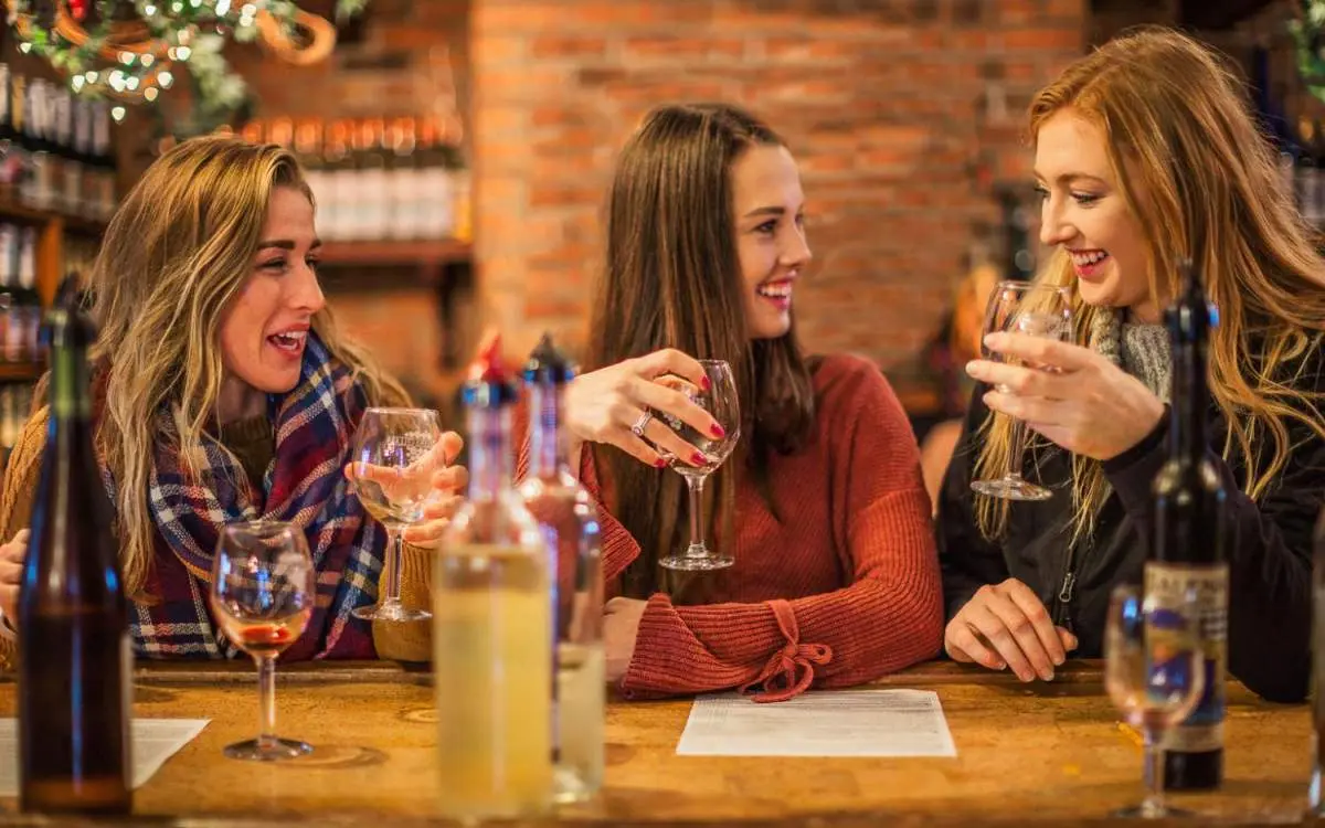 Tres mujeres sentadas a una mesa disfrutando de una copa de vino en el interior de una bodega
