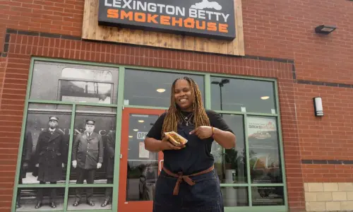 Una mujer sostiene un perrito caliente delante del ahumadero Lexington Betty Smokehouse.