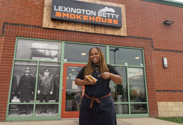 Una mujer sostiene un perrito caliente delante del ahumadero Lexington Betty Smokehouse.