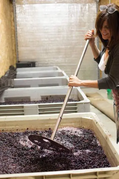 Una mujer mezcla las uvas en un gran recipiente para hacer vino.