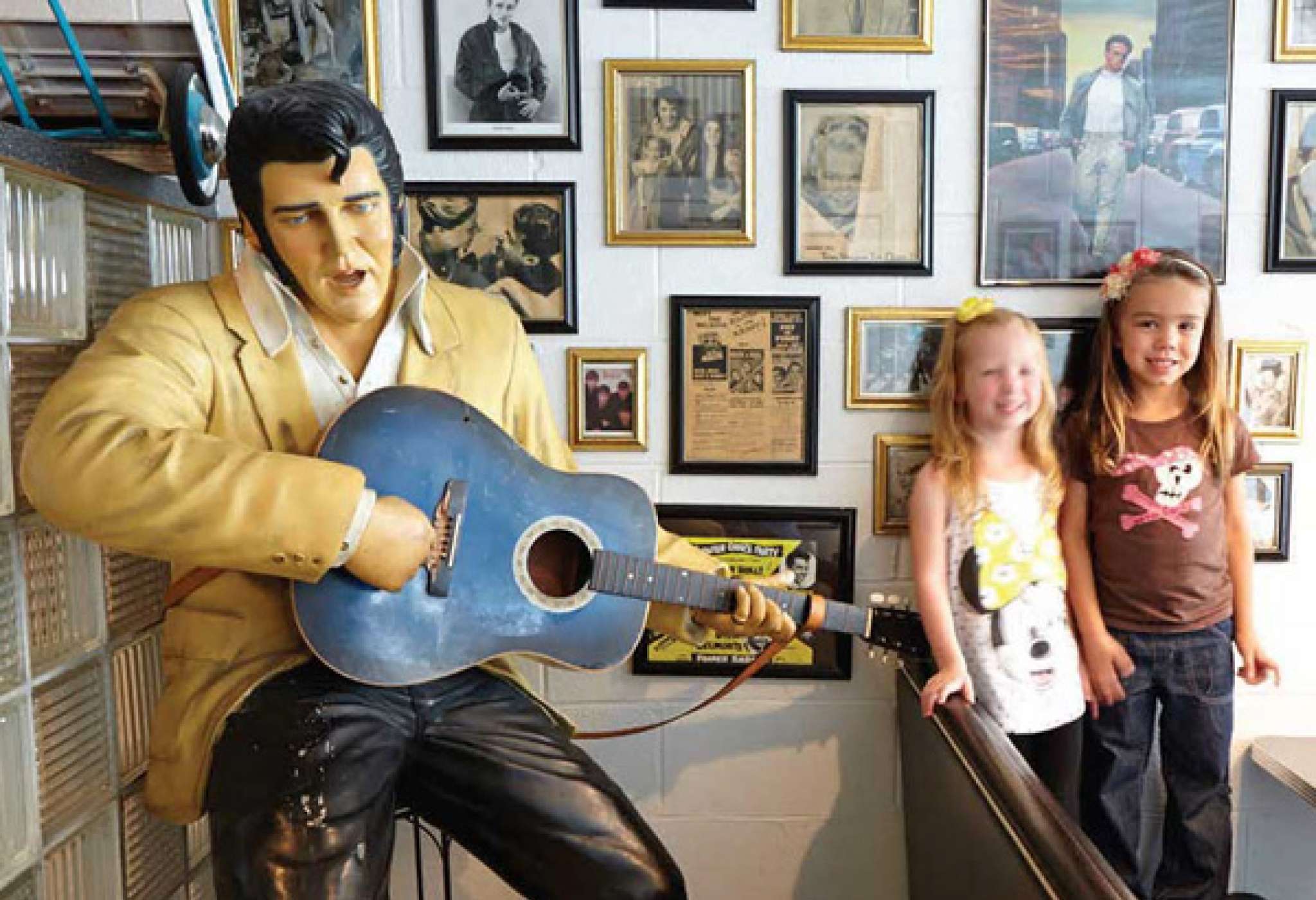 Dos niños se hacen una foto junto a una estatua de Elvis Presley con una guitarra en la mano. 