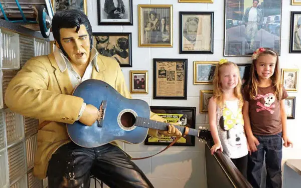 Dos niños se hacen una foto junto a una estatua de Elvis Presley con una guitarra en la mano.
