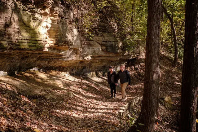 Dos personas caminando por el bosque junto a una gran roca