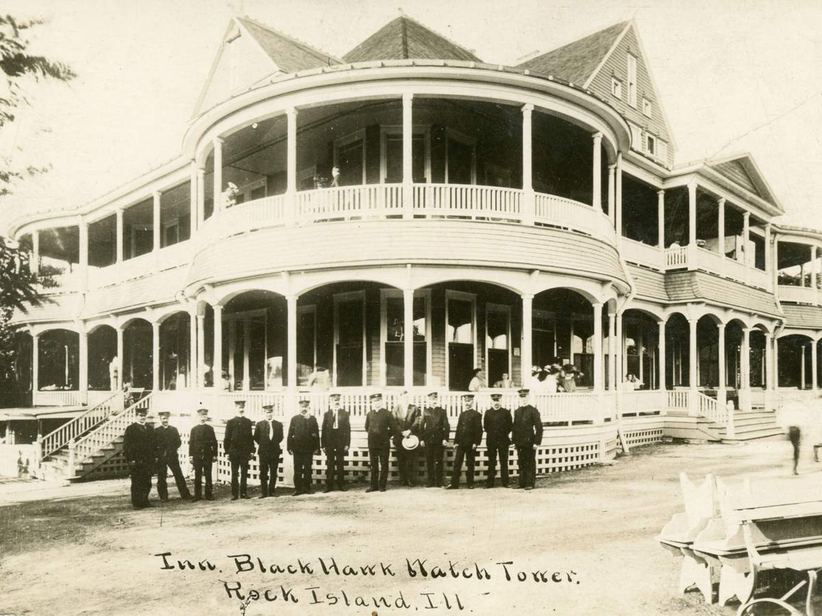 Foto antigua en blanco y negro de un grupo de hombres delante de un edificio de madera.