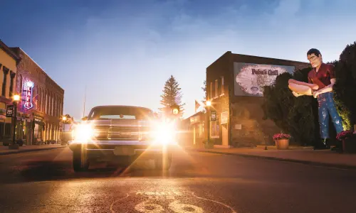 Un automóvil clásico con los faros encendidos, junto a la estatua gigante de Paul Bunyon en Atlanta