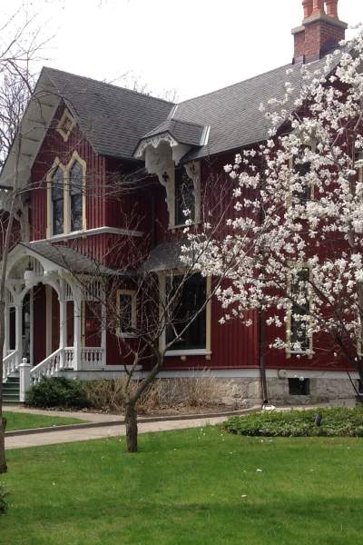 Una gran casa de madera roja de dos plantas del siglo XIX, detrás de un césped y un árbol en flor