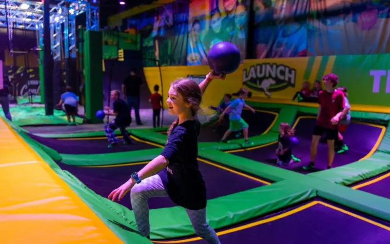 Una chica lanza un balón prisionero en un parque de trampolines cubierto