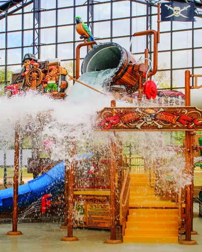 Un cubo salpica agua sobre una torre de juegos de temática pirata en un parque acuático cubierto.