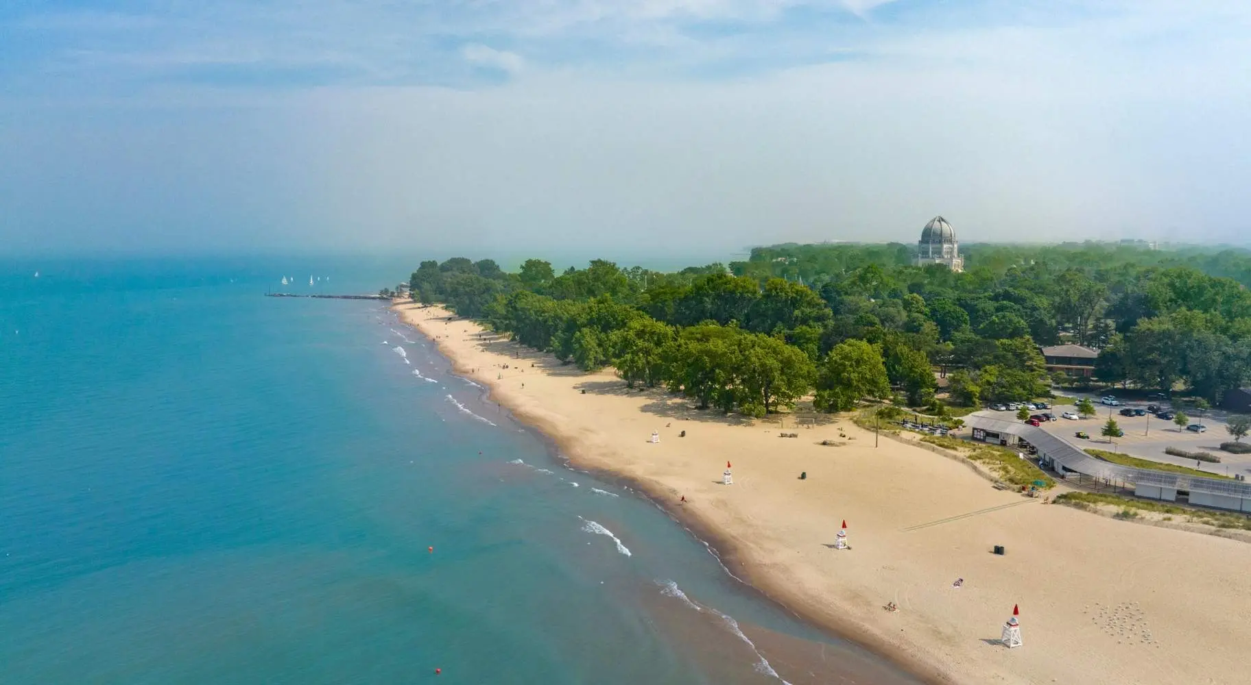 Una toma aérea de la costa de una playa, con árboles verdes al fondo