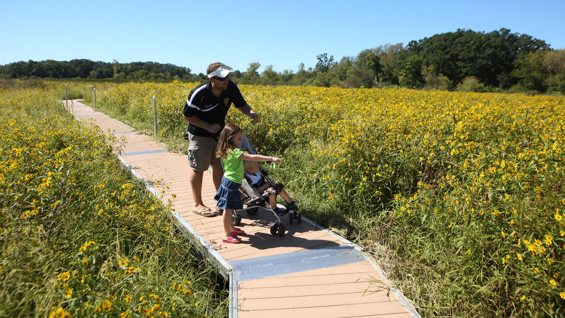 Un hombre con dos niños pequeños en un paseo marítimo entre flores amarillas