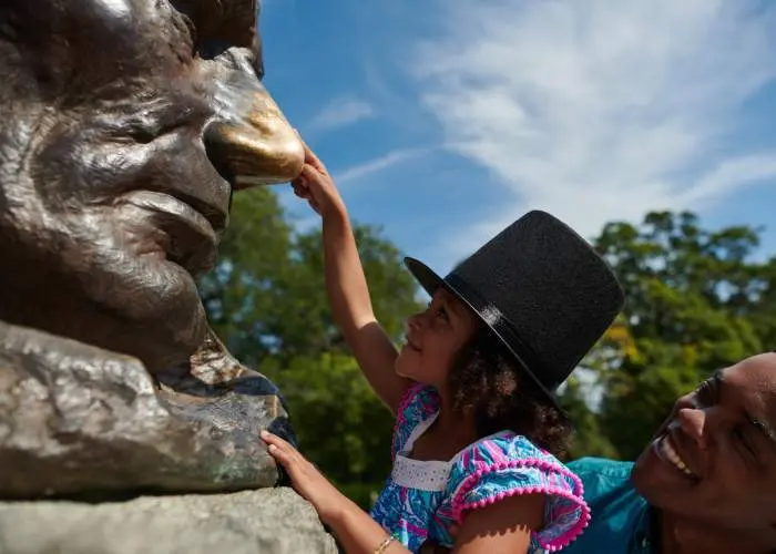 Un padre levanta a su hija para que toque la nariz de la estatua de Lincoln.