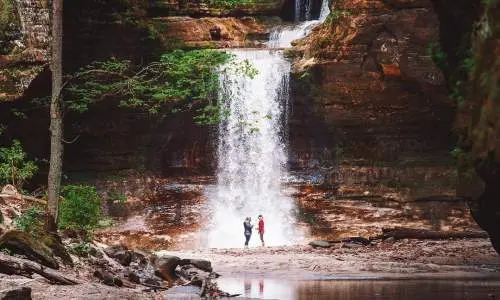 Dos personas de pie frente a una cascada, junto a un sereno estanque.