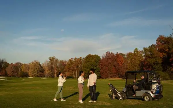 Amigos hablando en un campo de golf, junto a un carrito de golf