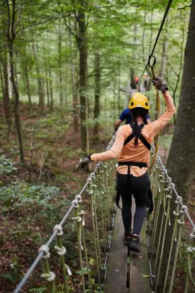 Personas en un puente que cruza los bosques con arneses y cascos de seguridad en Canopy Tours.