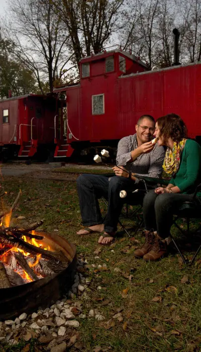 Pareja tostando malvaviscos en la hoguera con un tren detrás.