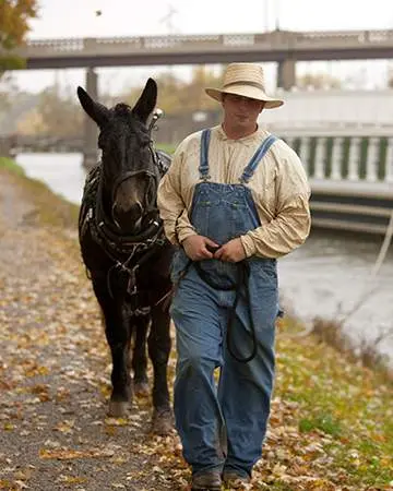 Hombre guiando un burro y una barca del canal