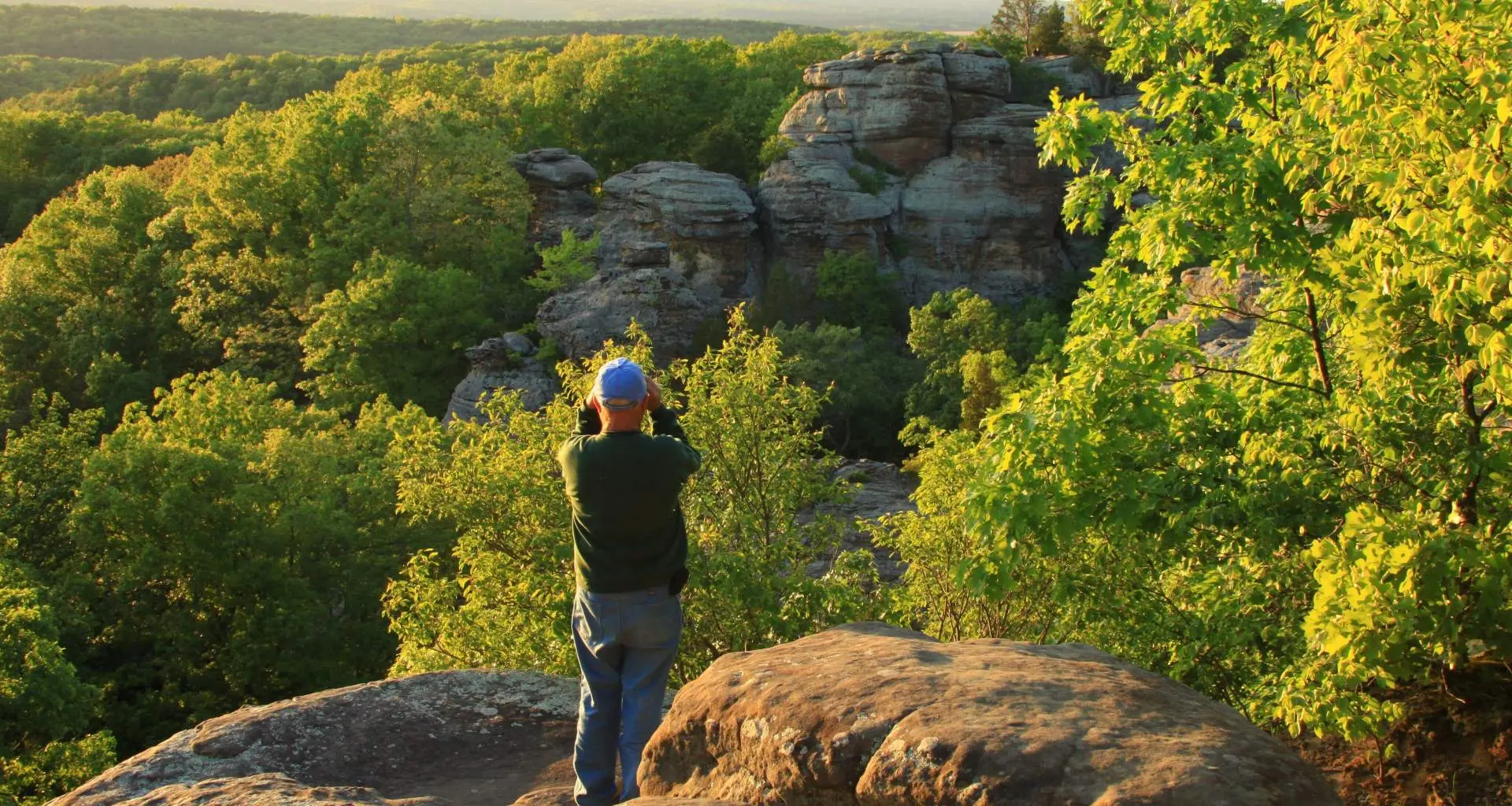 Un hombre en una roca con vistas a un bosque
