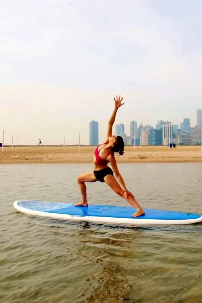 Mujer haciendo estiramientos sobre una tabla de paddle surf en un lago