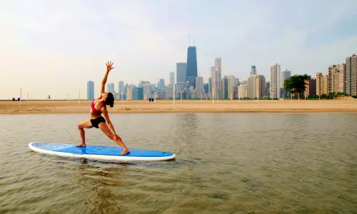 Mujer haciendo estiramientos sobre una tabla de paddle surf en un lago