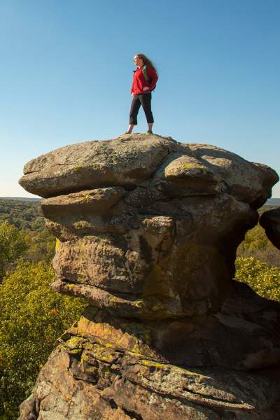 Mujer de pie sobre una gran roca con vistas al bosque.