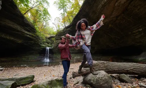 Dos personas trepando por las rocas frente a una cascada de roca