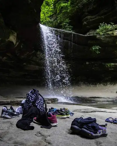 Una cascada desde una roca, con los bolsos y zapatos de la gente tirados en la roca de abajo