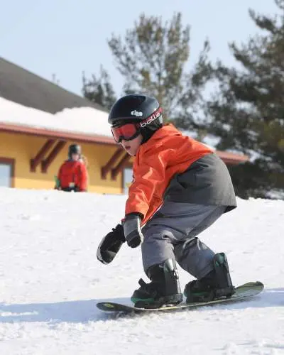 Un niño pequeño montando en snowboard sobre la nieve, con casco, gafas y ropa de esquí de abrigo.