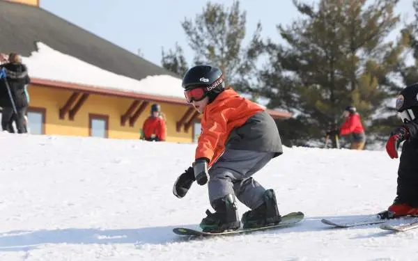 Un niño pequeño montando en snowboard sobre la nieve, con casco, gafas y ropa de esquí de abrigo.