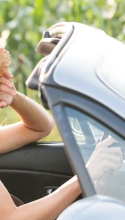 Girls in a convertible driving by corn fields.