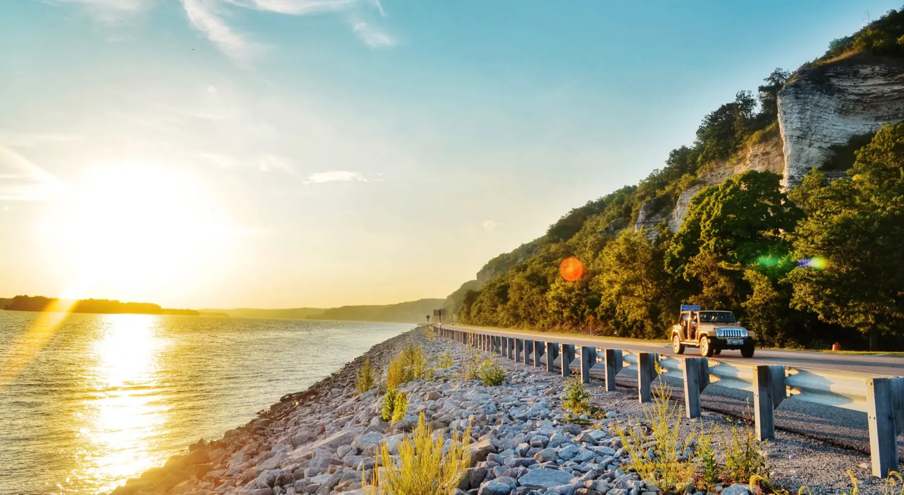 El amanecer brillando sobre el agua y un automóvil circulando por la carretera a su lado
