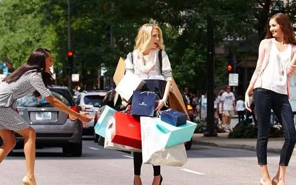 Mujer con un puñado de bolsas de la compra en medio de un paso de peatones.