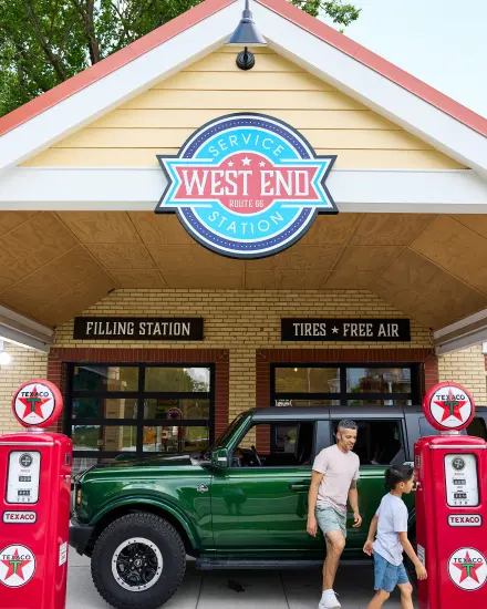 Un padre y su hijo pasan junto a un todoterreno verde y unos surtidores de gasolina antiguos en la estación de servicio West End, en la Ruta 66.