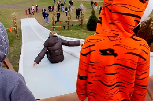 Un niño que lleva una sudadera con capucha naranja y negra espera para tirarse por el tobogán. 