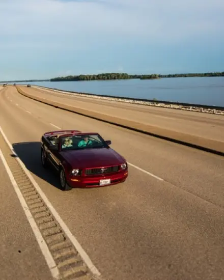 Un descapotable rojo circulando por una carretera panorámica junto al río Misisipi.